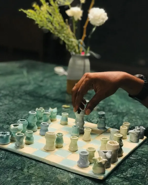 Game night, but make it art. A hand moves a piece on my "Cocoa Clash" ceramic chess set, which sits on a beautiful marble table. It's a functional sculpture that invites you to play.