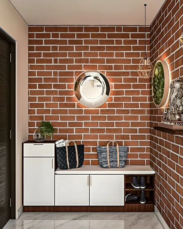 An industrial-chic entryway featuring a white storage bench with shoe compartments against a rustic red brick wall. A statement mirror and modern lighting complete the look.
