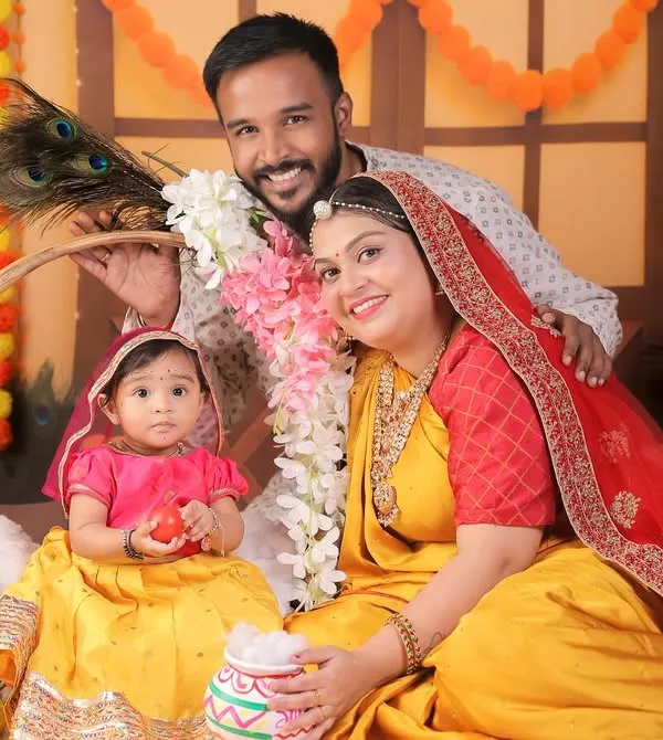 A lovely family portrait from a Radha-themed shoot, with parents and their 8-month-old daughter in coordinated traditional outfits.