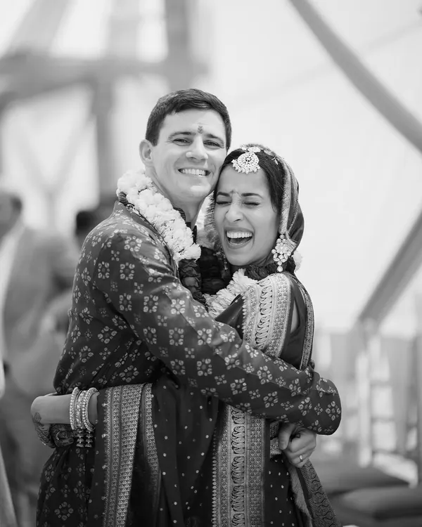 A joyful, candid moment captured in timeless black and white. This image of the American groom and Indian bride sharing a heartfelt laugh and embrace perfectly encapsulates the spirit of their union.