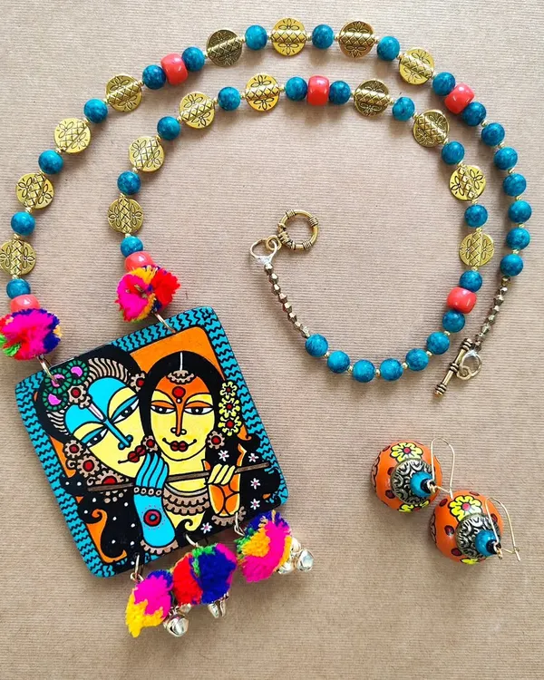 This Radha Krishna necklace set is one of my signature pieces, capturing divine love in bright, joyful colours. The hand-painted MDF pendant is complemented by matching wooden jhumkas, colourful pompoms, and brass embellishments, making it a complete work of wearable art.