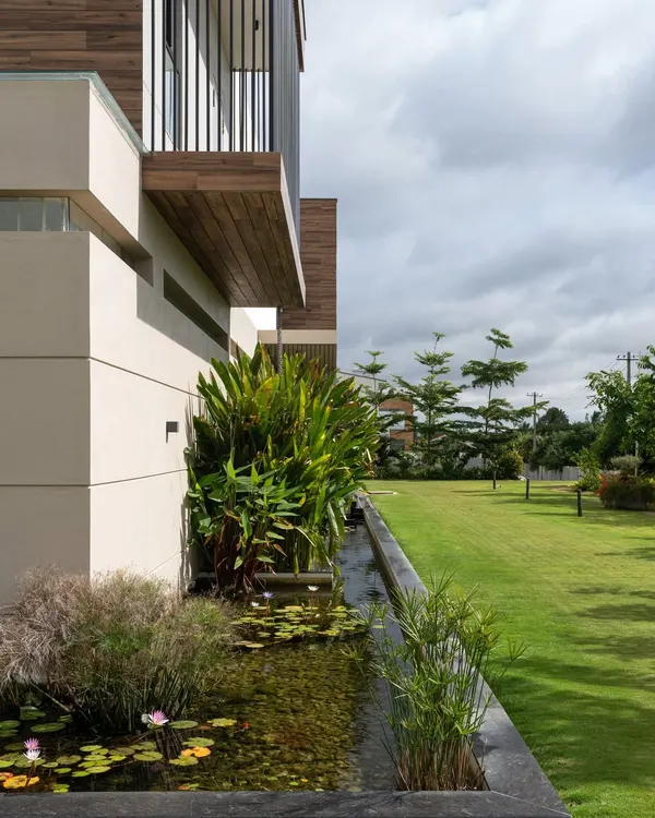 An exterior view of the Celadon residence, showing how the built form is nestled into the lush landscape. The koi pond wraps around the edge of the home, creating a natural moat that connects the structure to the garden.