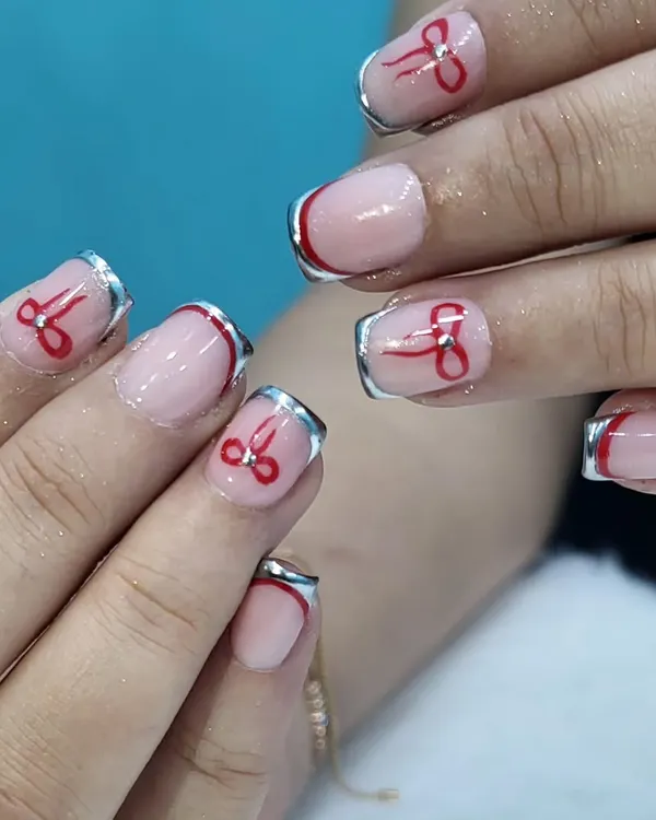 A playful twist on the French manicure, this design features a shiny chrome silver tip and a hand-painted red bow on each nail for a cute and quirky finish.