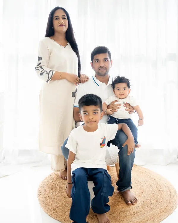 A classic family portrait with parents and two sons. The coordinated white and denim outfits and the bright, clean background create a timeless and fresh look.
