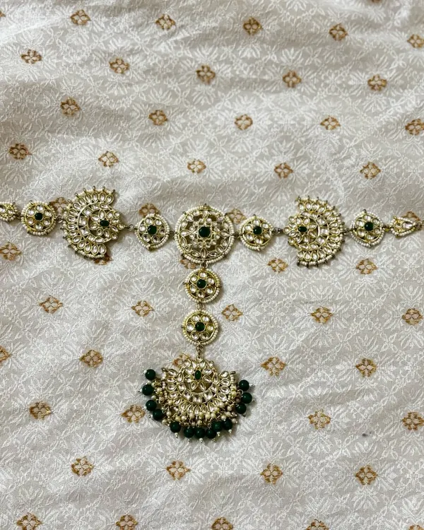 A traditional hair choti accessory for rent, designed with Kundan work and green beads to adorn a long braid.