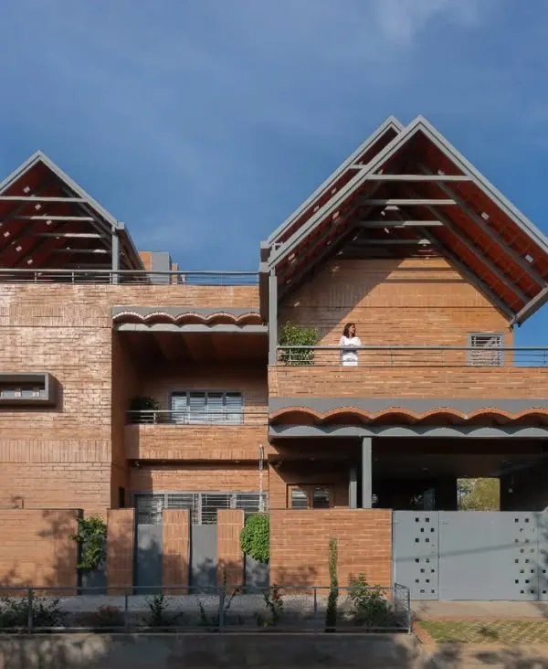 The Madhura residence features a distinctive facade with sloping tile roofs and walls made of CSEB mud blocks. The design merges two family homes on a single urban plot, using arches and vaults to create unique interior volumes.