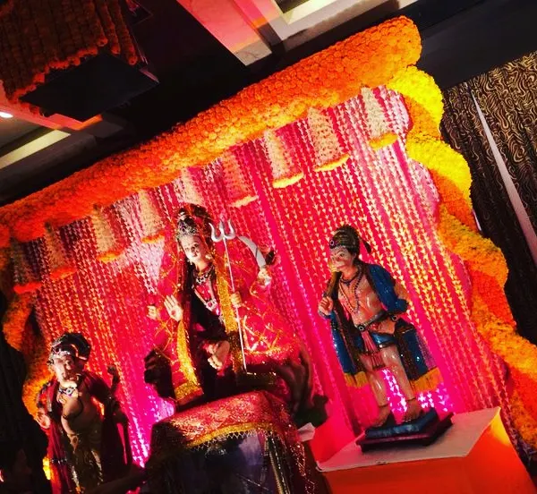 A traditional Mata ki Chowki decor setup. This features a backdrop of flower strings and a heavy arch of orange marigolds, creating a sacred space for worship in a club house or at your chosen venue.