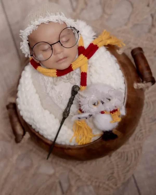 Welcome to the wizarding world, little one. This creative Harry Potter themed newborn shoot features a sleeping baby with iconic glasses, a Gryffindor scarf, and a magic wand, showing how we bring your favorite stories to life.