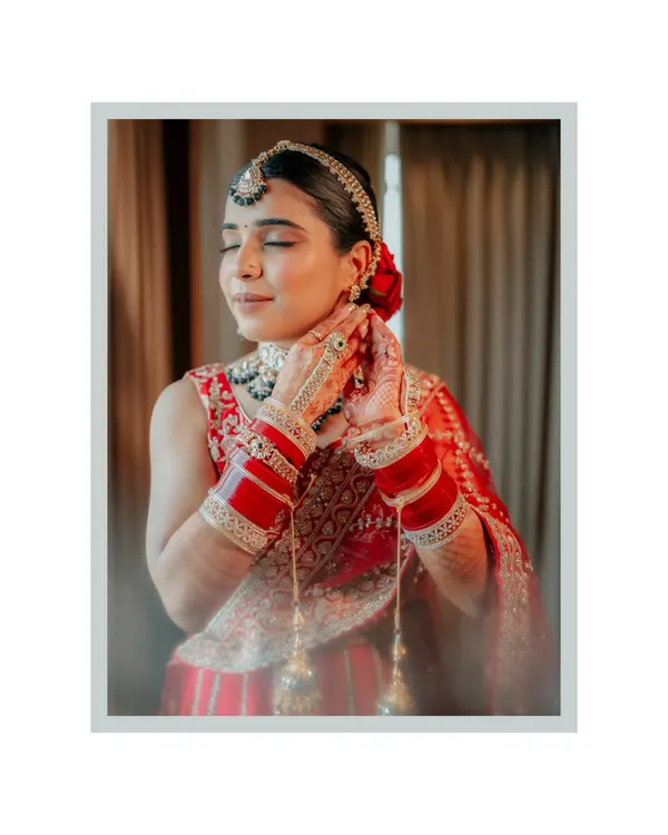 A serene moment as the bride, Neha, closes her eyes, adjusting her earring. The soft lighting and her traditional red attire create a timeless and beautiful portrait.