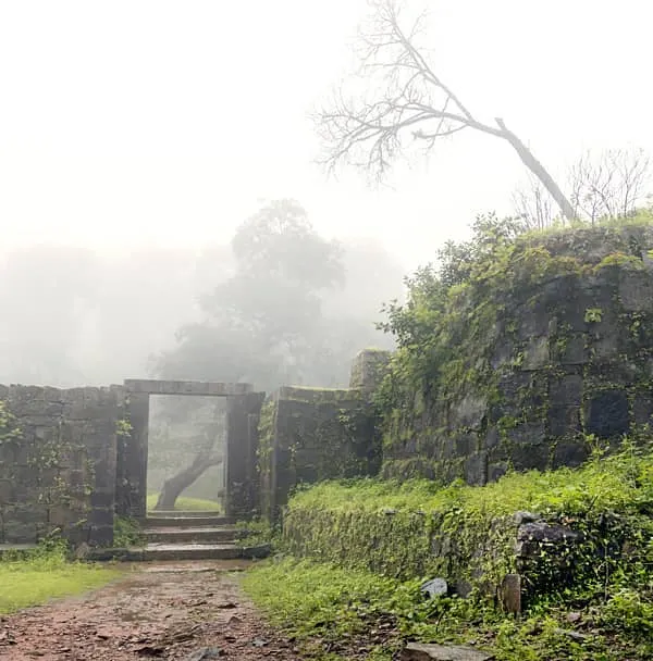 The ruins of Kavaledurga Fort on a foggy day. The thick mist covering the landscape gives the ancient stone structures a mysterious and haunting feeling, perfect for a moody fine art photograph.