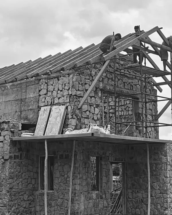 A house takes shape with walls of natural, random rubble stone. Here, workers are installing the wooden framework for a traditional sloping roof, a process that requires precision and teamwork.