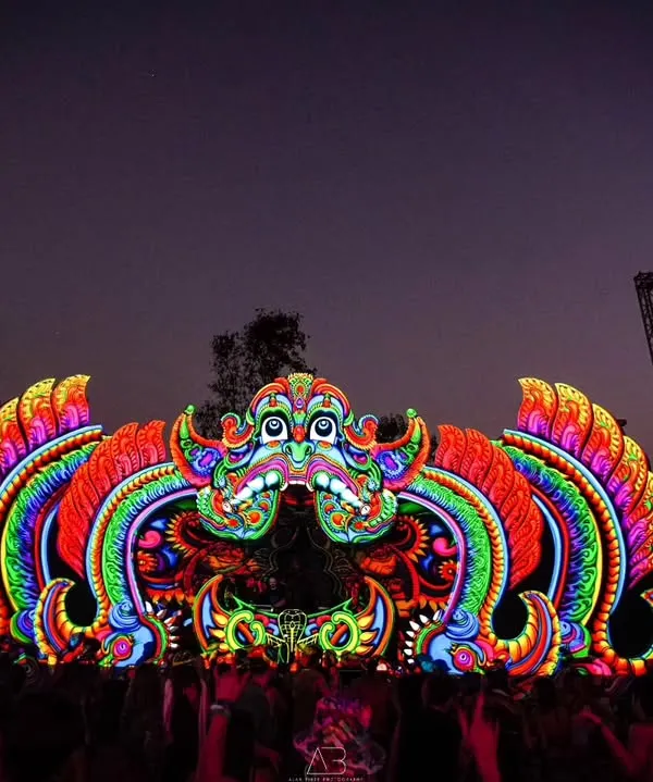 The main stage of a Goa trance music festival at night. The vibrant, psychedelic decor is lit up, showcasing the epic scale and electric atmosphere of the event.