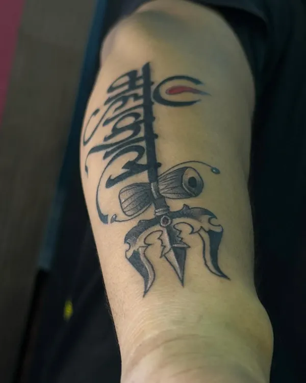 A powerful Mahakal trishul tattoo for the upper arm. This design combines the sacred trident with a damaru and calligraphic lettering, creating a classic spiritual statement.