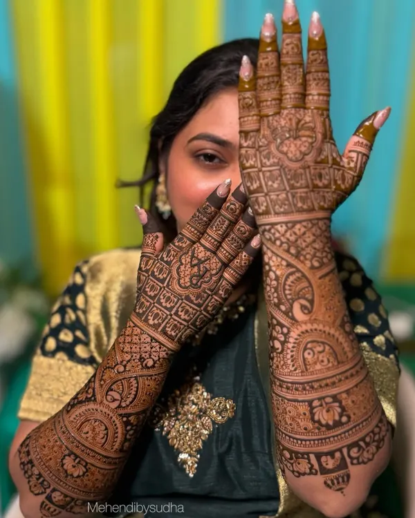 A beautiful bride, Rutuja, showcasing her full bridal mehendi. The design is packed with traditional elements, including intricate jaali (net) patterns, peacocks, and floral bands.