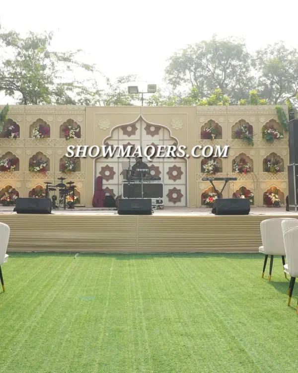 A full view of a stage designed with a "Banaras" theme. The backdrop features intricate archways and niches filled with flowers, creating a culturally rich setting for a daytime corporate event or dealer meet.