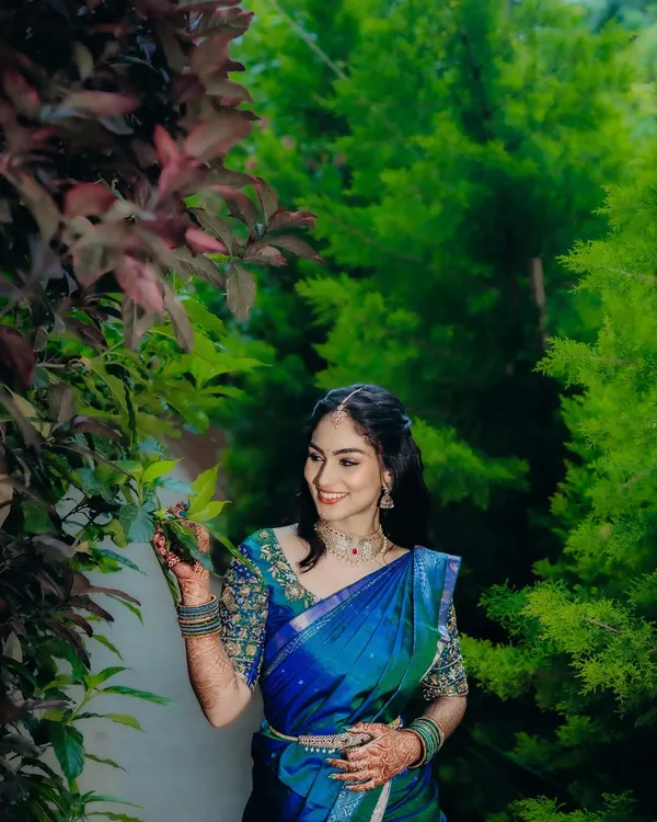 A beautiful outdoor shot of the bride-to-be. The natural greenery provides a stunning backdrop for her vibrant blue and green saree and the soft, glowing makeup I created for her engagement.