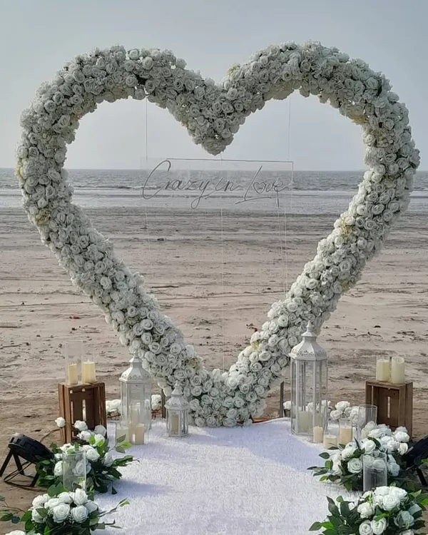 A breathtaking beach proposal setup in Mumbai, featuring a custom heart-shaped arch of white flowers and a 'Crazy in Love' neon sign. We designed this to create a truly magical and picture-perfect moment for the couple.