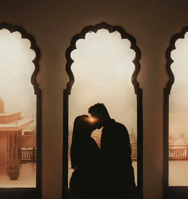 A silhouette of a couple kissing, perfectly framed by three ornate arches against a soft, warm background. This shot captures a timeless, romantic moment with an artistic and dramatic flair.