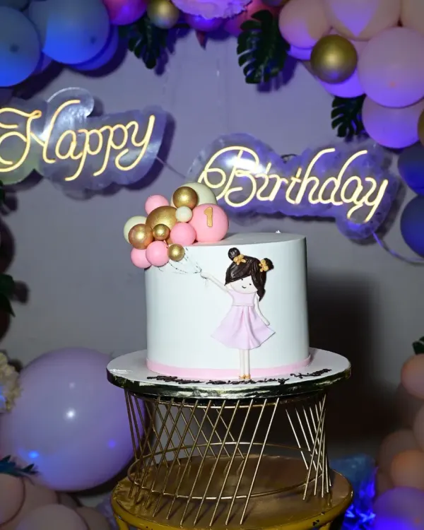 A chic and modern birthday cake setup. The simple, elegant cake is perfectly complemented by a gold wire stand and a stylish neon "Happy Birthday" sign.