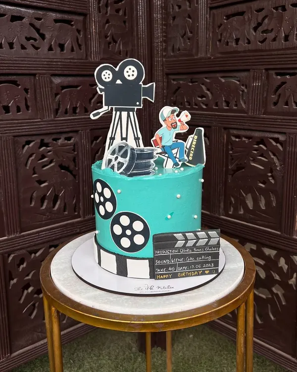 Lights, camera, action! This movie director-themed cake is perfect for a film enthusiast, complete with a camera, film reels, and a personalized clapperboard, all made from edible materials.