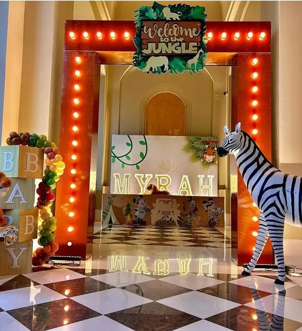 Welcome to the jungle! This grand entrance features a marquee-lit archway, life-sized zebra and tiger props, and a personalized light-up name display for "Myrah," creating an exciting start to the safari adventure.