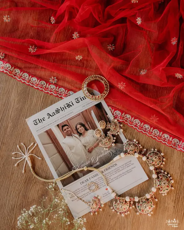 A flat lay of the bride's accessories, including her jewelry and a custom newspaper invitation, set against her red wedding veil.