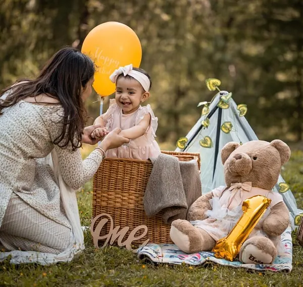A beautiful, candid moment as a mother shares a laugh with her daughter on her first birthday. The outdoor setting in the mountains provides a stunning, natural backdrop for these family interactions.