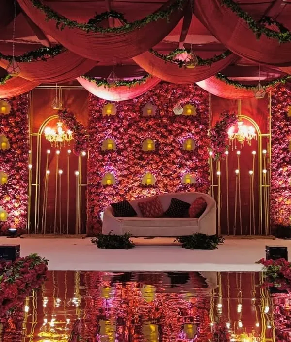 A stage that is a symbol of timeless elegance. We created this opulent backdrop with layers of plush red fabrics, a wall of cascading florals, and warm golden accents for a truly grand reception.