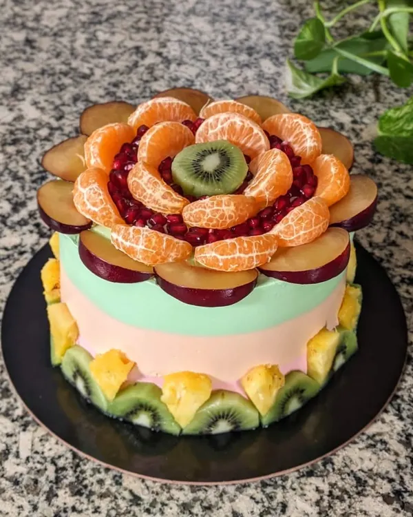 Fruits are nature's candies! This fruit-overloaded cake features a beautiful floral arrangement of plums, oranges, pomegranates, and kiwi on a tri-color cream frosting.