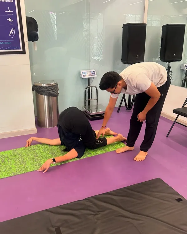 A student practices Halasana (Plow Pose) in my gym class. I'm providing a gentle adjustment to help her deepen the pose and release tension in her neck and shoulders.