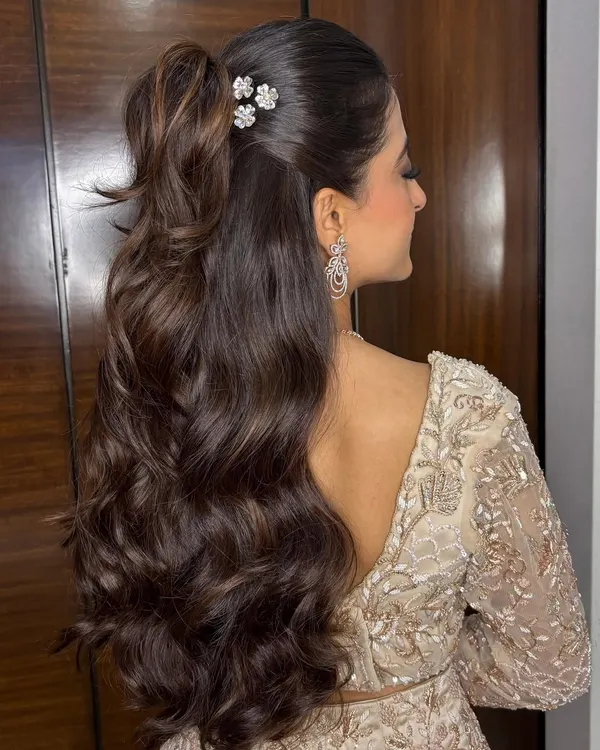 A glamorous half-up ponytail with voluminous, cascading waves and delicate floral clips. This style is perfect for a cocktail party or reception, offering a look that is both chic and modern.