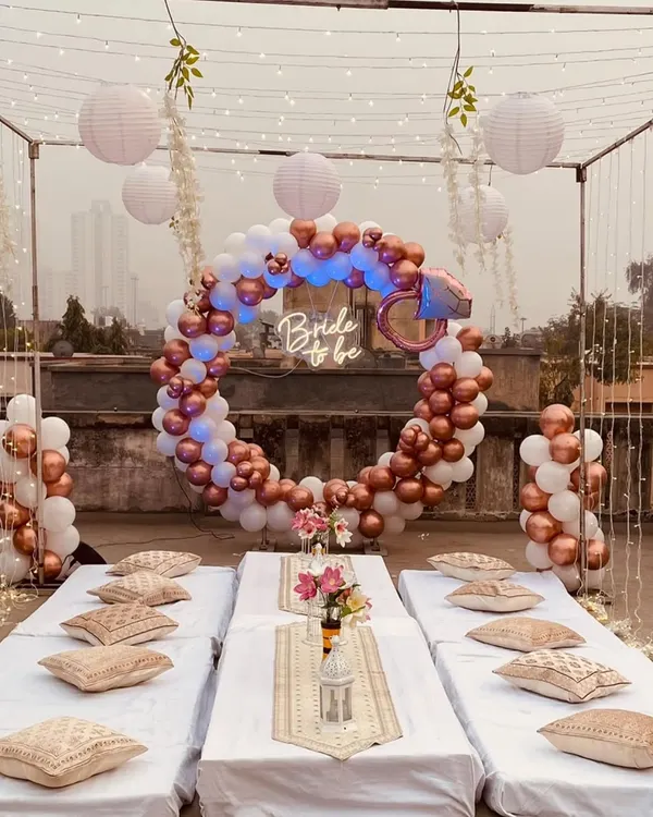 We transformed this Bengaluru terrace into a chic bachelorette party lounge. The setup features a stunning circular balloon arch in rose gold and white, a custom "Bride to be" neon sign, and elegant low seating for an unforgettable evening celebration.