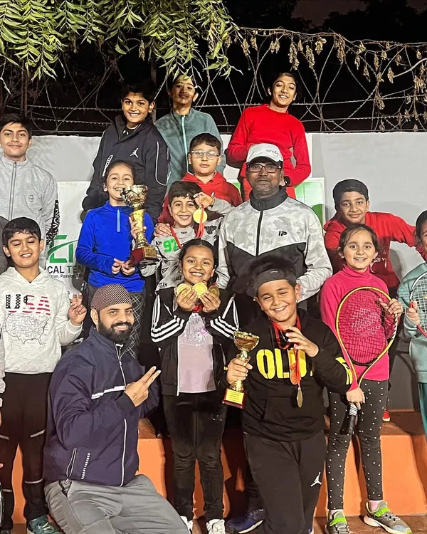 The future of tennis is bright. Here is a large group of our junior players and coaches celebrating their wins at an open tournament, with everyone beaming with pride, holding their trophies and medals.