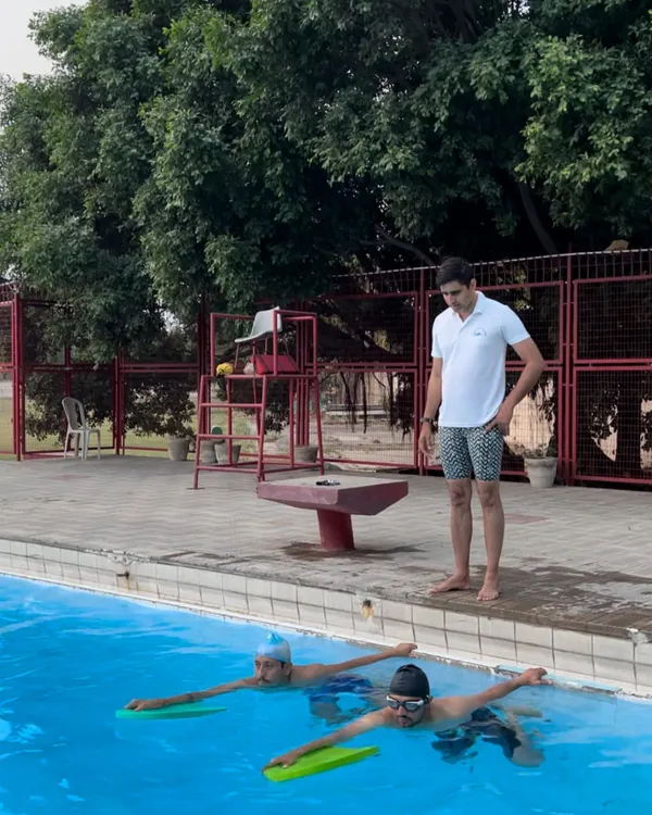 A coach provides poolside guidance as swimmers use kickboards. This close supervision is a core part of our method, ensuring you get the feedback needed to refine your swimming form.