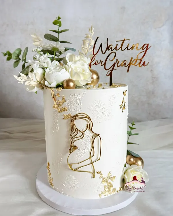 A sophisticated and elegant baby shower cake. The design is clean and modern, with textured white buttercream, gold leaf, and a beautiful "Waiting for Grapin" topper.