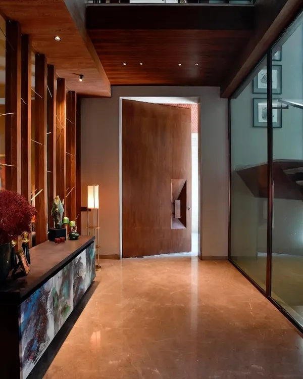 The entrance to a contemporary Gurgaon home, featuring a massive, custom-designed wooden pivot door. The adjoining console and art piece set a tone of sophisticated, artistic living from the moment you step inside.