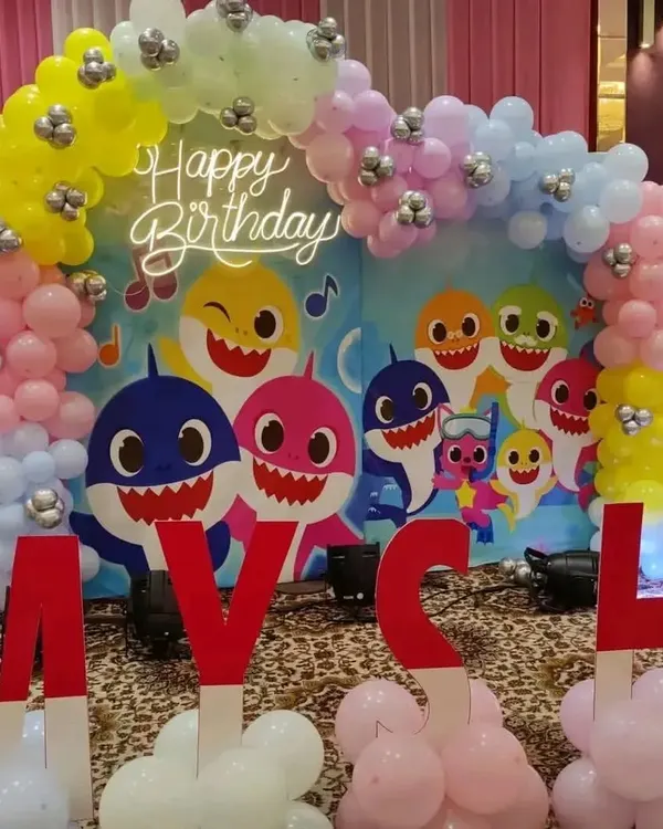 A colorful Baby Shark themed birthday party, featuring a character backdrop, a pastel balloon arch, and large custom letters.