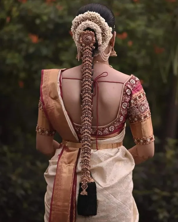 A stunning view of a bride's back, showcasing both her intricate hairstyle and our custom blouse. The blouse features a deep back with detailed embroidery along the borders, designed to be seen and admired.