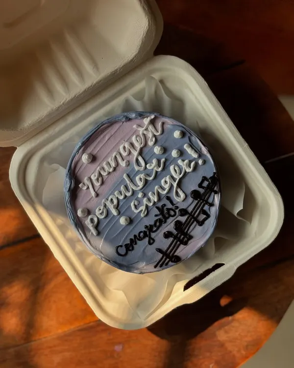 A congratulatory bento cake for a "young popular singer." The cake features a purple and blue ombre design with musical notes to celebrate a special achievement.