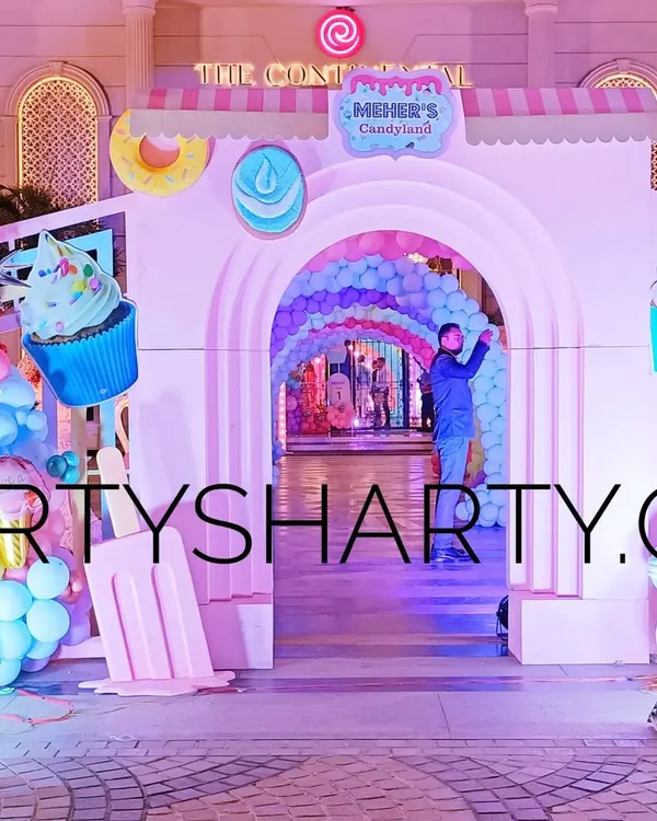 A spectacular entrance to a 'Candyland' party, with giant cupcake and ice cream props, and a tunnel of rainbow balloon arches.