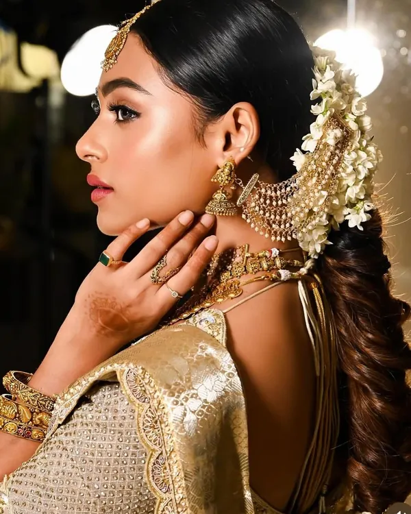 A side profile showcasing a traditional South Indian bridal hairstyle. This look features a thick, textured fishtail braid adorned with classic temple jewellery and fragrant jasmine flowers, creating a timeless and elegant silhouette for the wedding ceremony.