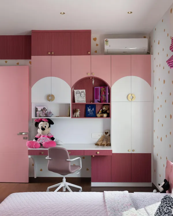 The completed kid's room from our Lakshya project. The design features custom cabinetry with an integrated desk and playful arched details, all in a charming pink and white palette with gold accents.