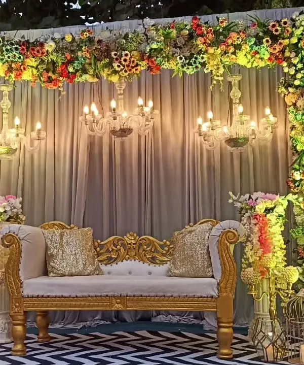 This is the kind of grand, floral stage I love to create for receptions. The setup features a full arch of multi-colored flowers, elegant chandeliers providing warm light, and a classic gold and white diwan for the couple, all set against a stylish chevron pattern floor.
