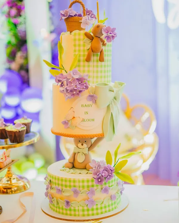 I believe the dessert table should be as beautiful as the main decor. Here, I've styled a stunning multi-tiered 'Baby in Bloom' cake, ensuring it perfectly matches the green gingham and lavender floral theme of the celebration.