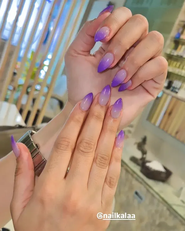 A beautiful purple ombre on sharp stiletto nails. The color fades perfectly from a sheer nude at the base to a vibrant violet at the tip for a striking and elegant look.