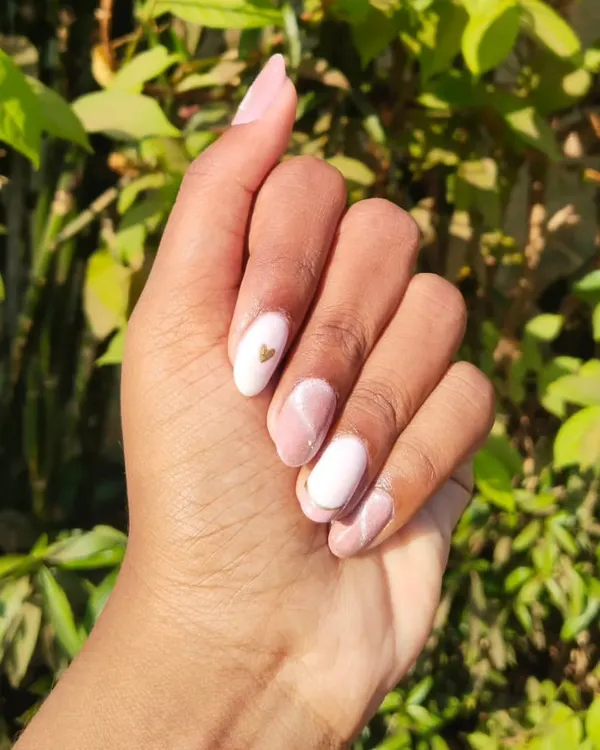 A soft and elegant gel polish set on natural nails. This design features a mix of solid white, a pink marble effect, and a tiny gold heart accent. It's a beautiful example of minimalist nail art.