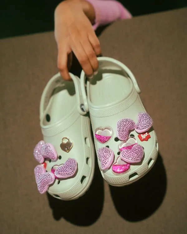 A creative product-focused shot for Crocs. Holding the shoes up to the camera highlights the customizable Jibbitz charms, showing the fun and personalizable aspect of the product.