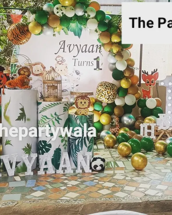 An amazing outdoor jungle safari party! The decorations look fantastic in a garden setting. The setup includes a custom backdrop, animal cutouts, and themed pedestals.