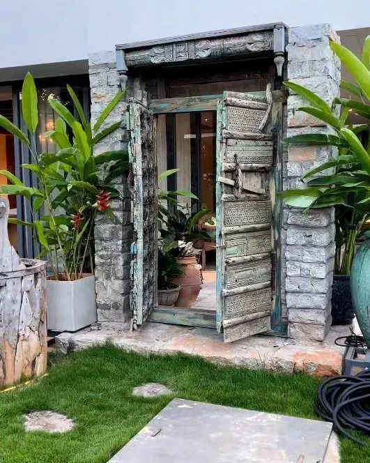 A closer look at the antique door feature. The weathered texture of the wood and stone creates a stunning contrast with the fresh green lawn, making it a true statement piece.
