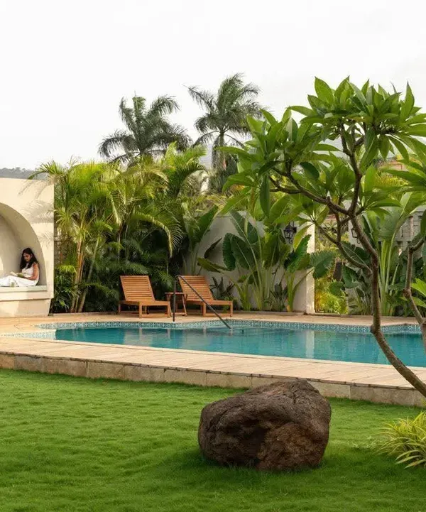 A poolside relaxation nook set against a backdrop of tropical palms and a pristine lawn. This design focuses on creating a private, resort-style oasis in a residential backyard.